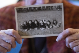 Barbara Lea Couphos holding a B&W photo of six women