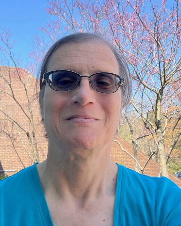 Woman with sunglasses and teal shirt smiles at the camera.