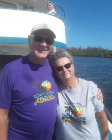 Man in purple shirt and baseball cap smiles next to woman in grey t-shirt