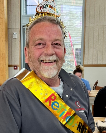 Man with hat and retirement sash smiles at the camera.