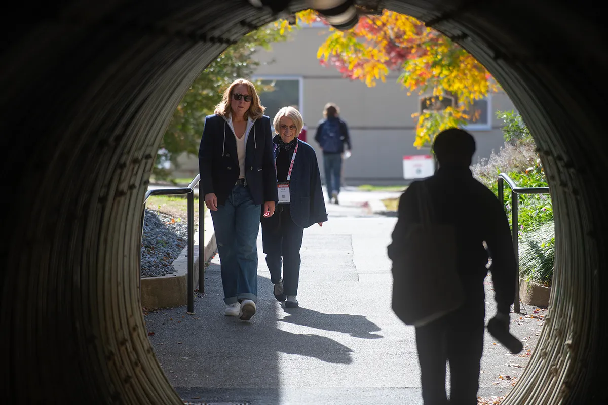 People walk through tunnel with fall foliage in background