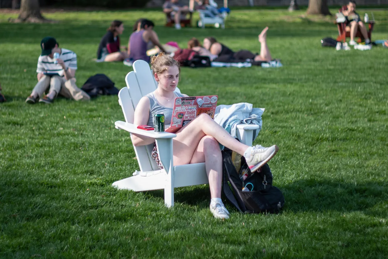 Student sits on white Adirondack chair and uses laptop