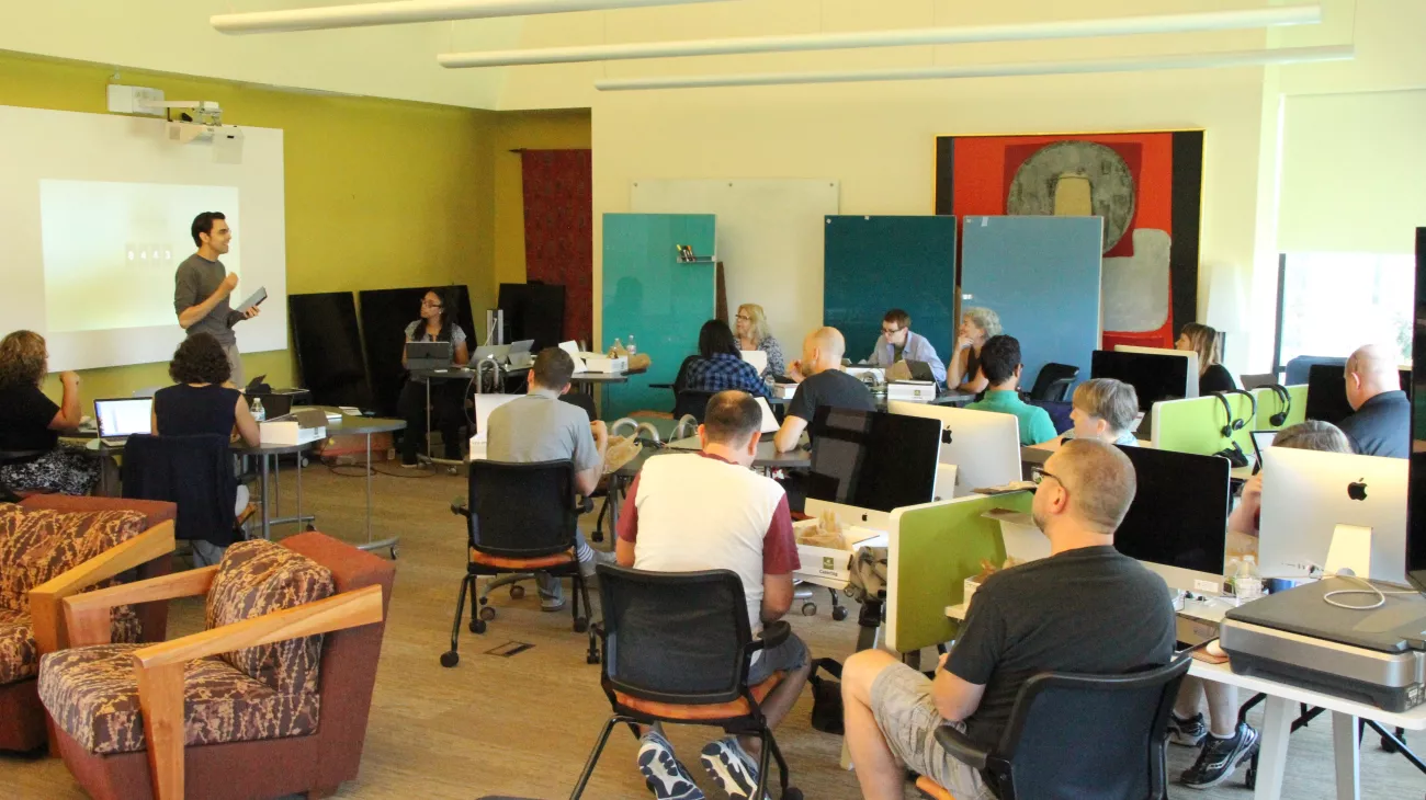 people sitting in a classroom with computers watching a professor present about teaching with an iPad