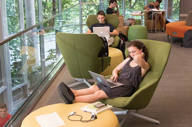 student studying in a soft chair in Cornell Library near a window