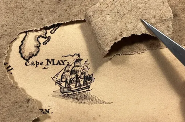 a tweezers gently pulls on the backing of an 18th century map to reveal a formerly hidden ink drawing of a ship on the reverse.