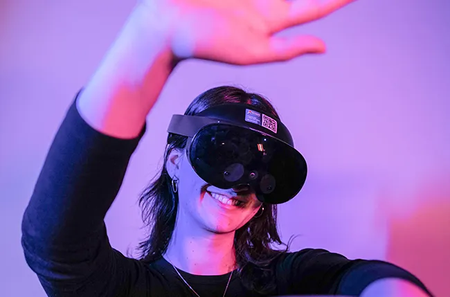 Emerging Technologies Fellow Liz Hogrefe against a purple background wearing a VR headset and moving her arms