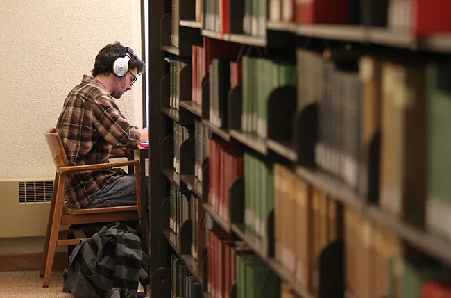 student wearing headphones studies in a thesis carrel in McCabe Library