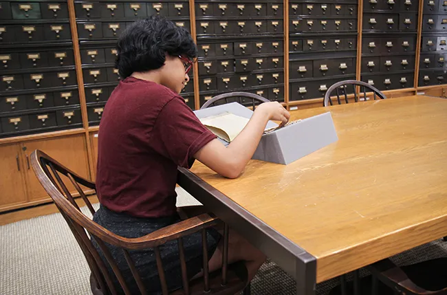 student seated at a table in the reading room doing research with an item from the collection