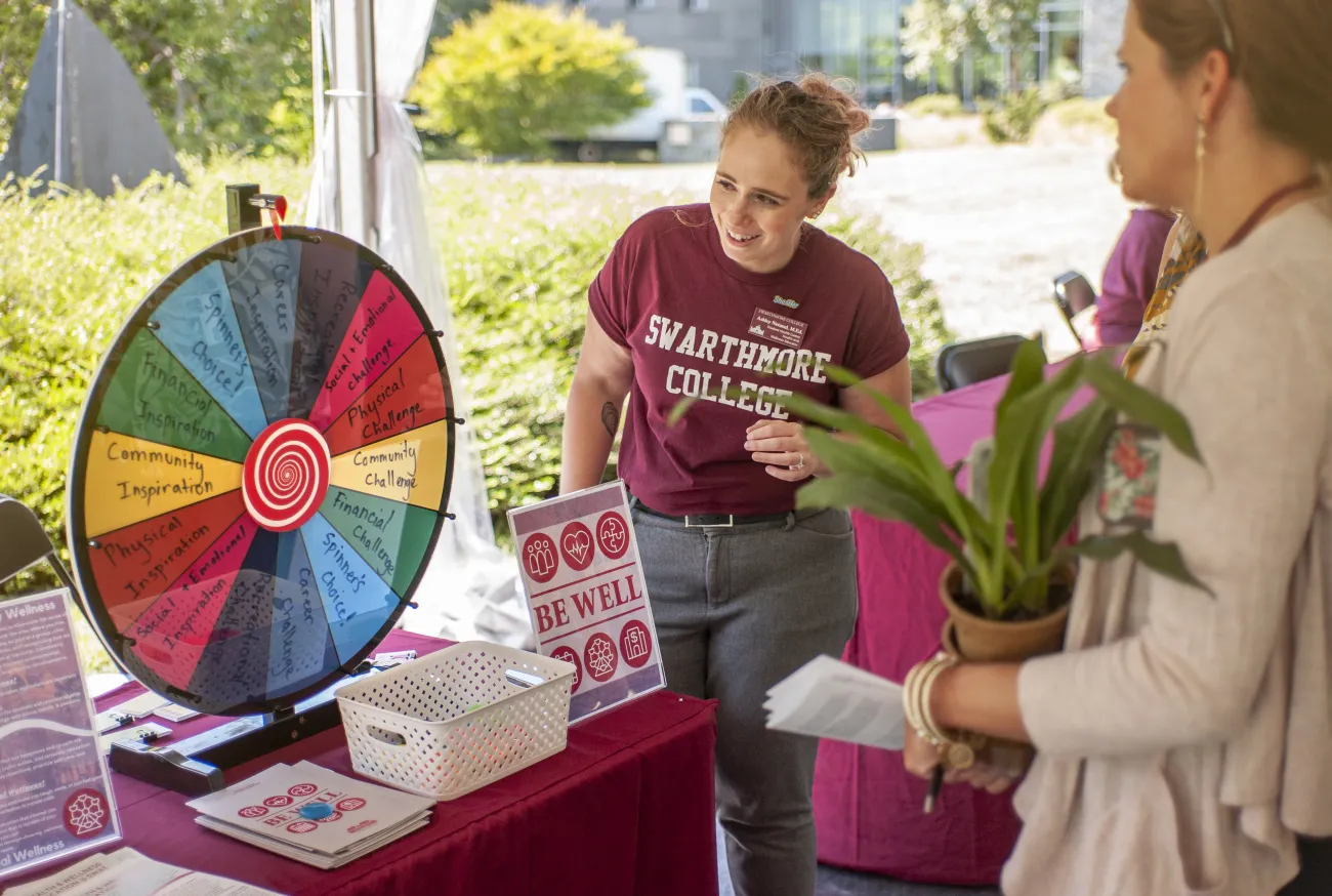 Staff member playing a wheel game of chance with a student holding a plant