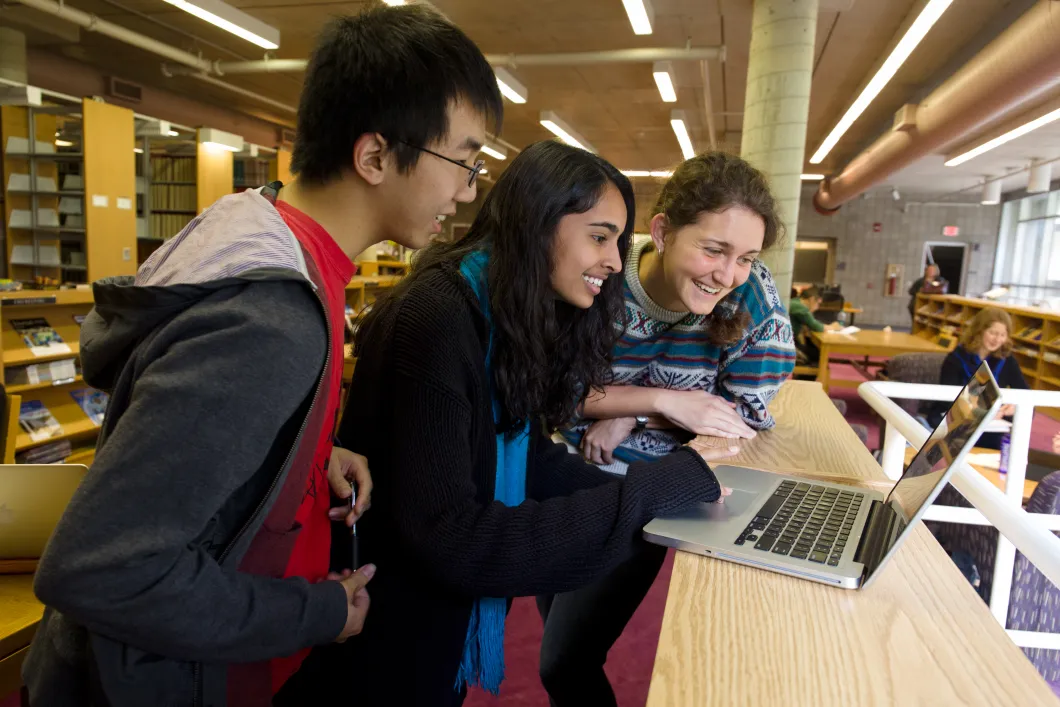 Three students looking at a computer together, smiling