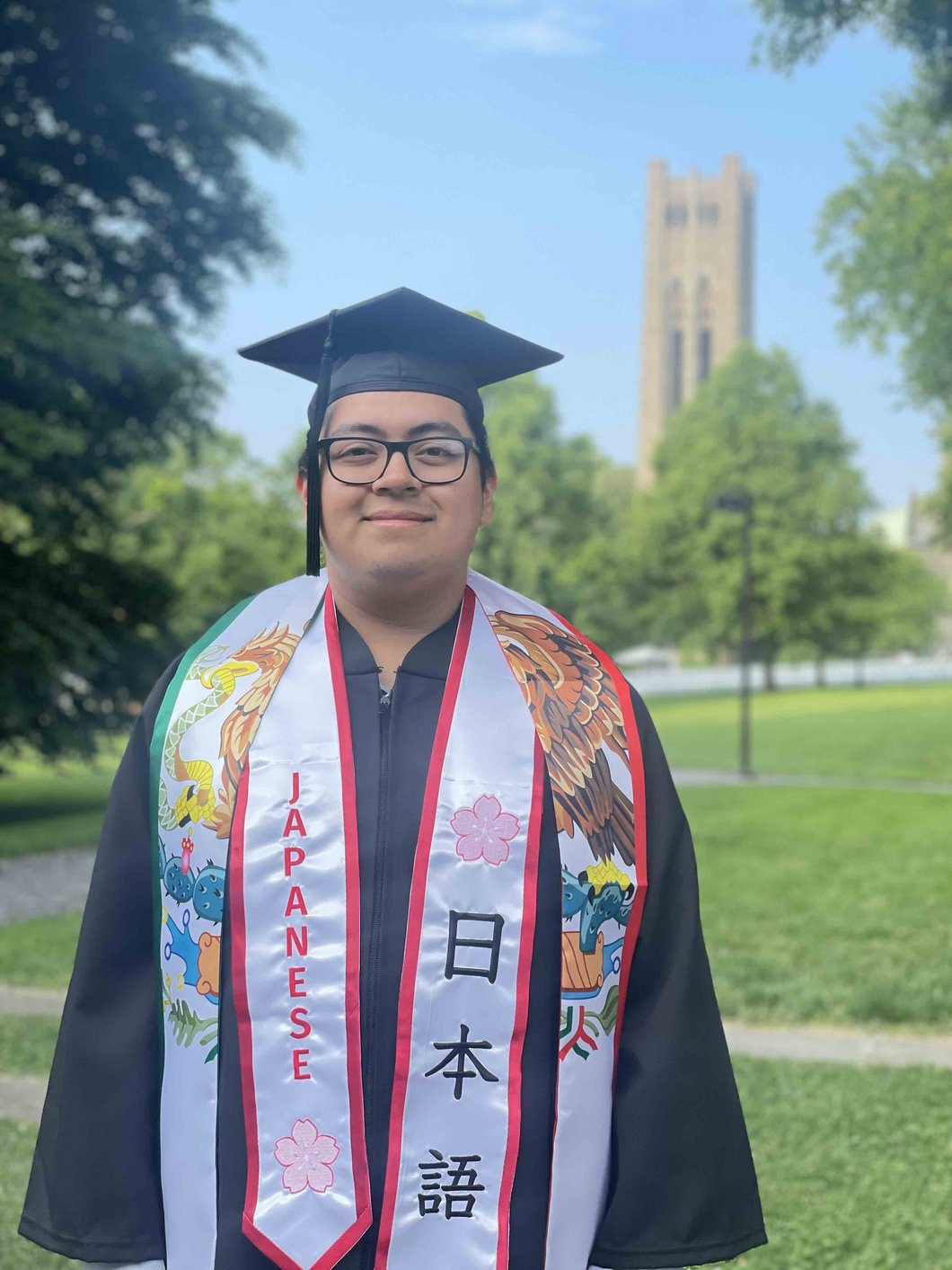 Japanese section graduate with cap and gown standing in front of Clothier Bell Tower