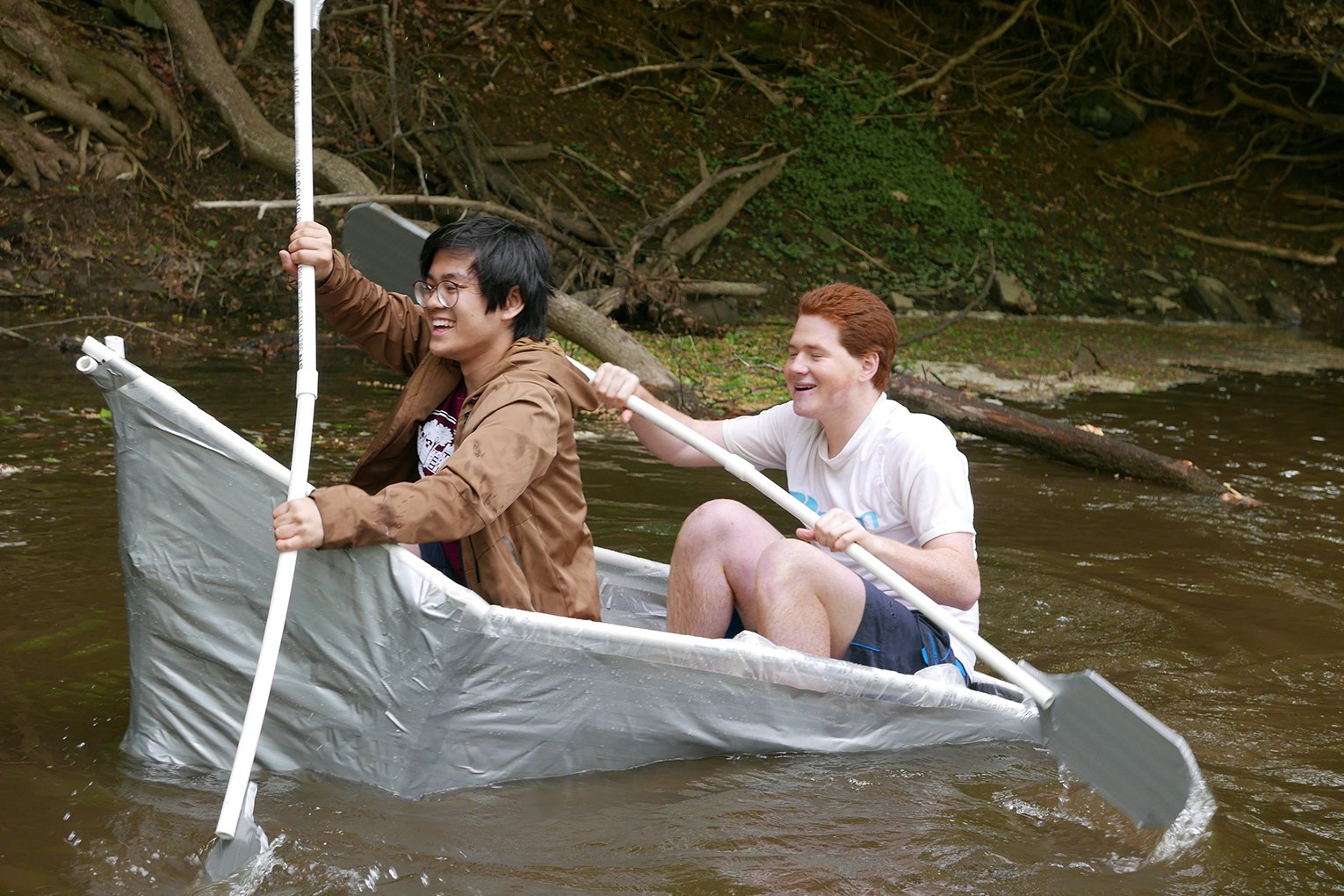 Students in makeshift boat on creek