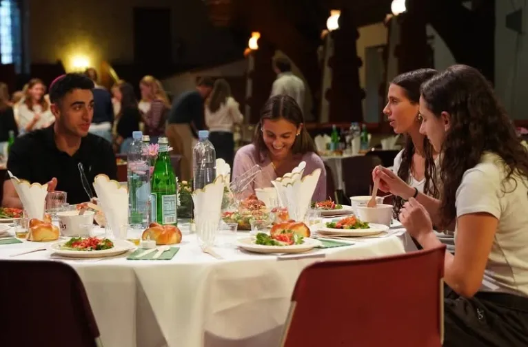 Four students sitting around a table sharing a meal and laughing.