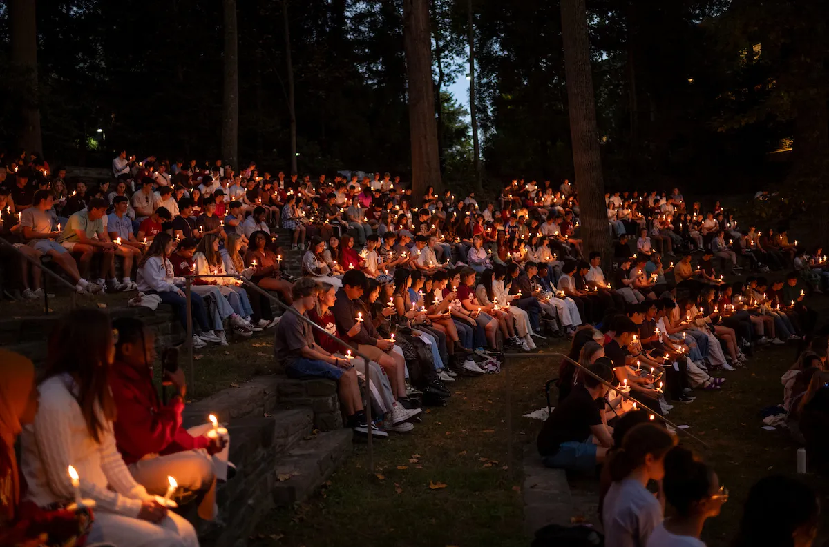 Students hold candles in outdoor amphitheater during collection