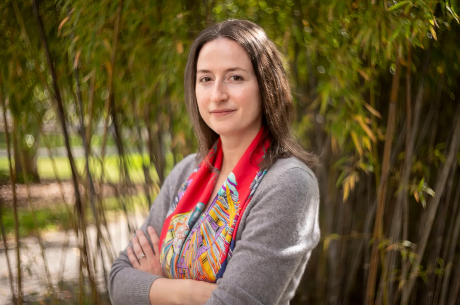 Jennifer Peck stands outside in front of bamboo plant with arms crossed