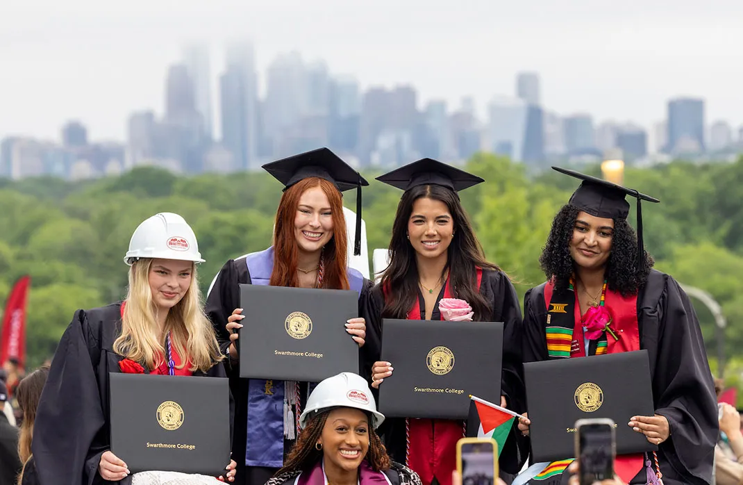 four graduates holding their diplomas with the Philadelphia skyline in the background