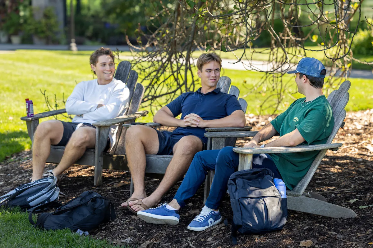 Students talk while sitting in Adirondack chairs