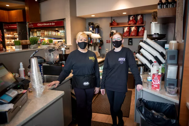 Two masked employees stand in cafe