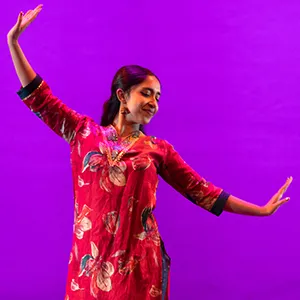 Dancer in red garb poses on stage in front of purple backdrop