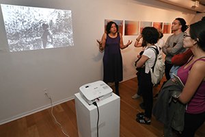 Baki Mani stands in front of projector while talking to class