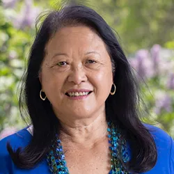 Amy Cheng Vollmer in blue top standing outside in front of blooming flowers