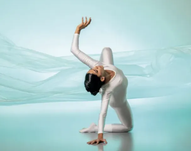 Person in white unitard dancing in front of blue green background