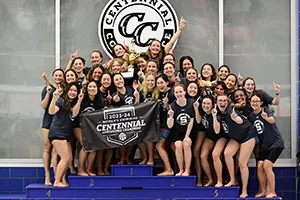 women's swimming team stands on podium celebrating conference championship with banner