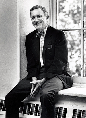 Charles Gilbert wearing suit and bowtie, sitting on a windowsill