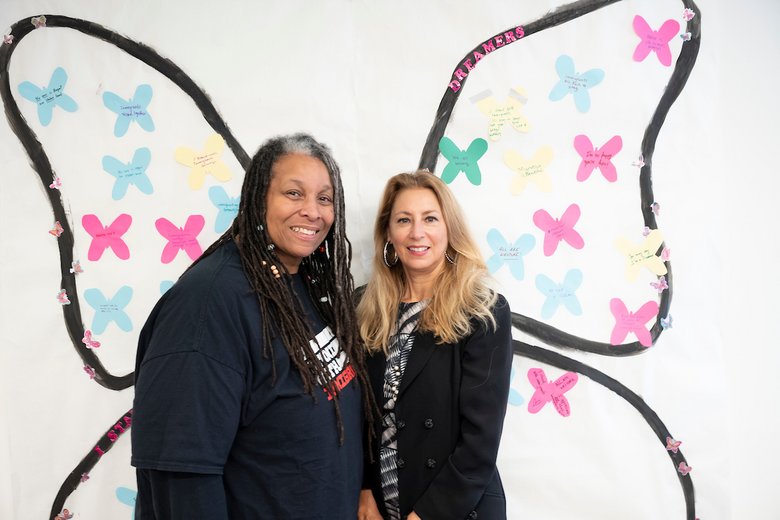 Deans Karen Henry and Jennifer Marks-Gold pose in front of a butterfly display