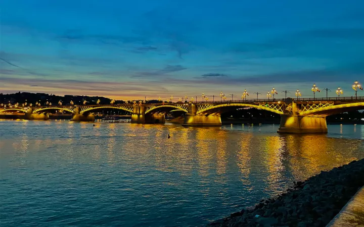 Bridge over large body of water at dusk, with bright yellow lights that are visible in reflection