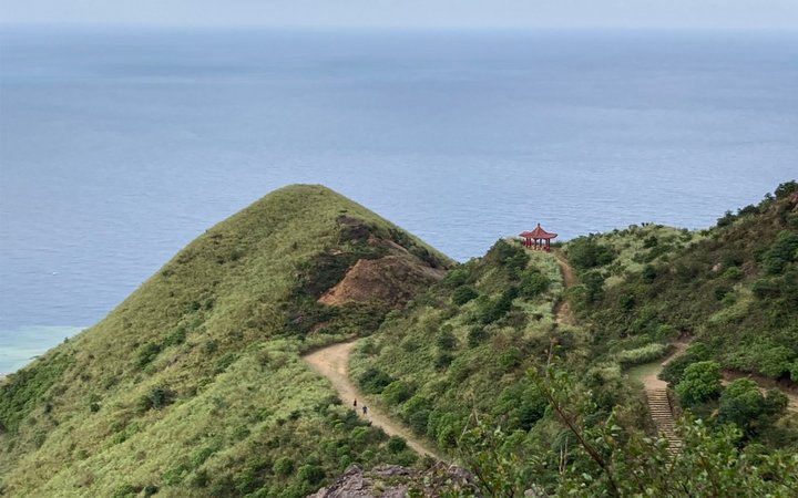 Grassy hill with tiny red shrine overlooking ocean
