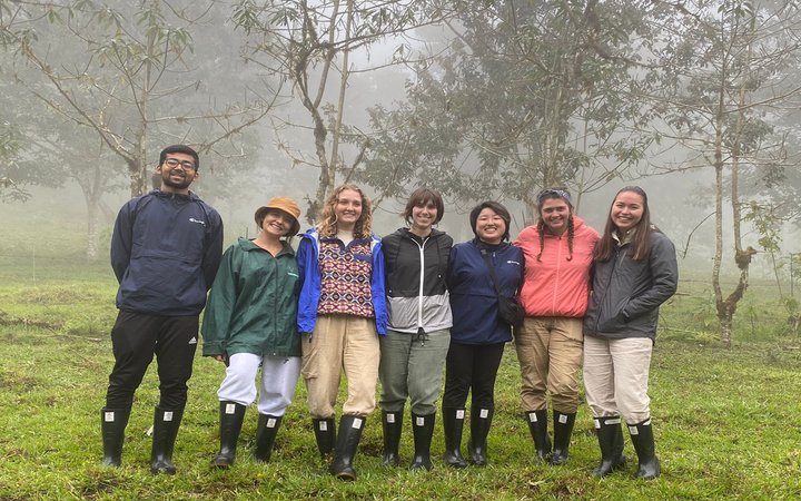 Group wearing raincoats and matching rain boots in front of misty forest