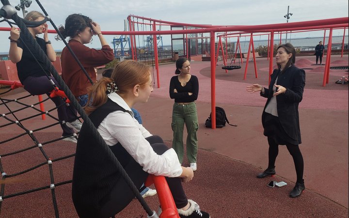 Group sitting on equipment in playground with ocean in background