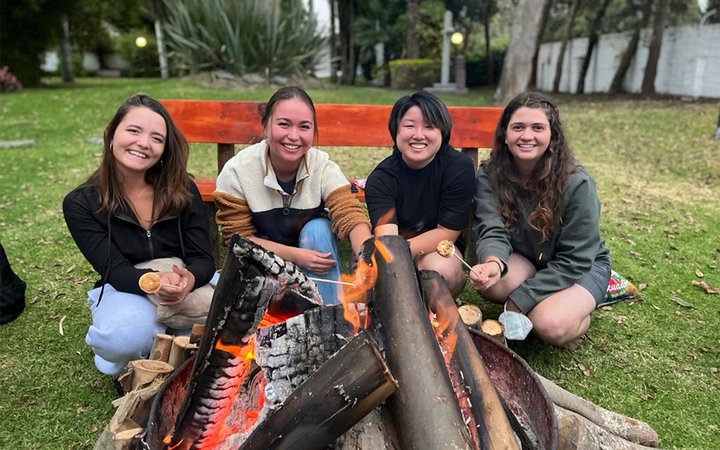 Four students smiling in front of a fire pit in a field