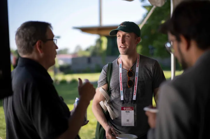 Three alumni have conversation in shade during outdoor reception