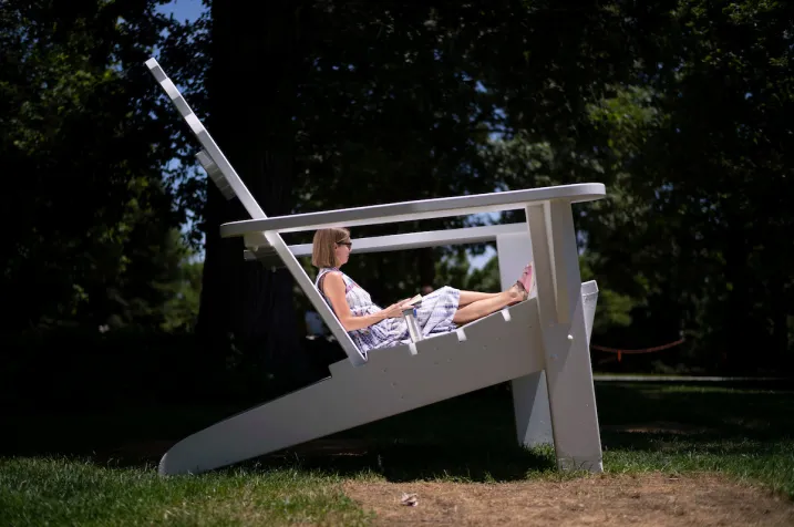 Person sits in large white Adirondack chair on lawn