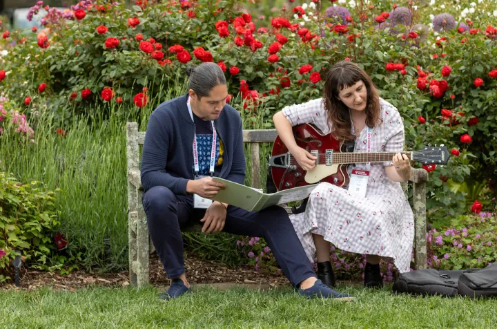 Alums sit on bench and woman plays guita