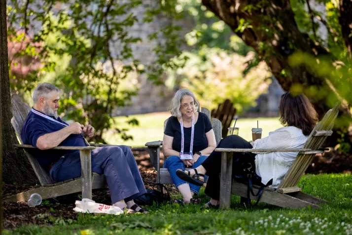 Alumni sit in small circle on adirondack chairs