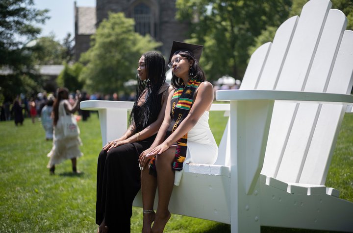 Two grads pose on large white chair