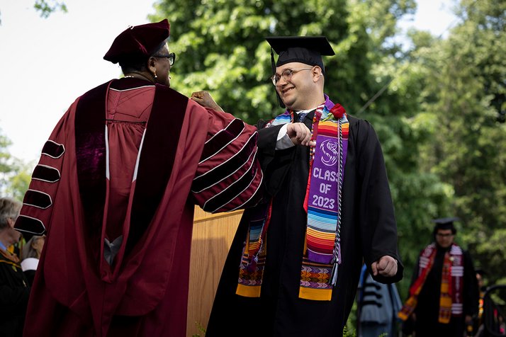 President Valerie Smith and a student touch elbows and smile on stage