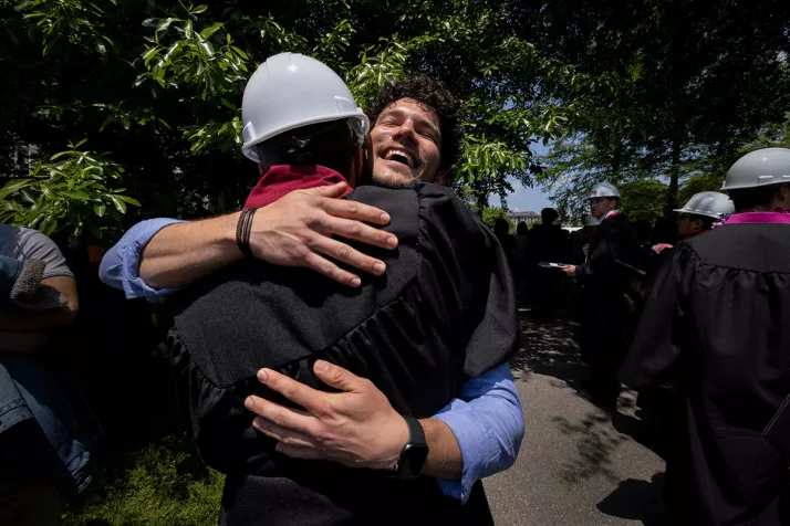 Student wearing engineering hard hat hugs friend after graduation