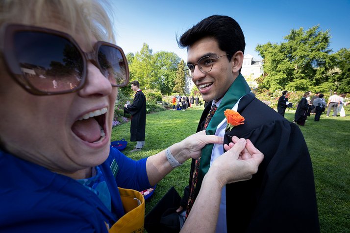 A woman happy pinning a rose to a student's gown