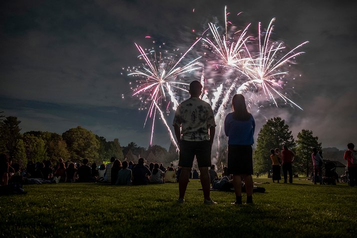 Two people stand and watch fireworks from a distance