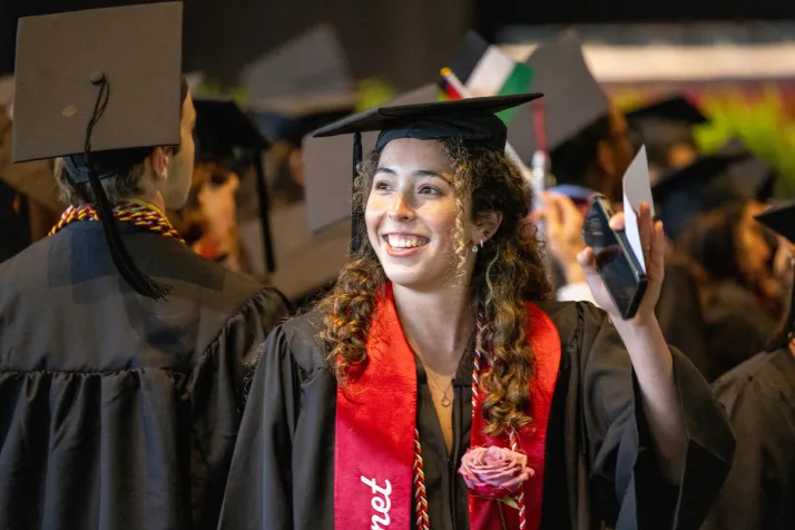 Student smiles and waves at crowd during graduation procession