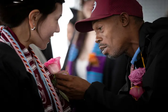 Person helps student with flower on commencement robe