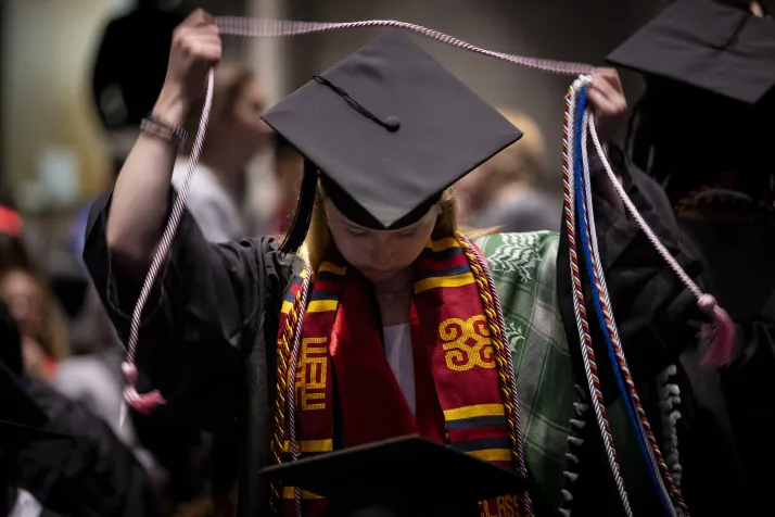 Student puts on cord while wearing commencement robe