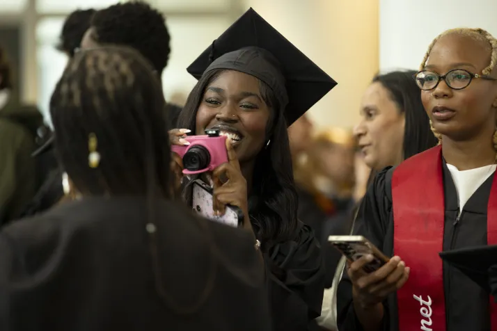 Student with disposable camera takes picture of another student while wearing commencement robes