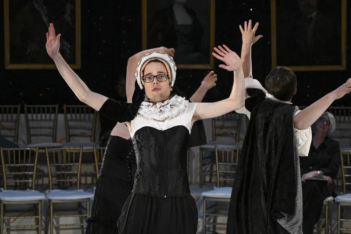 Frank Paz faces out with his hands over his head. He is wearing a nun's habit, and a white lace collar 