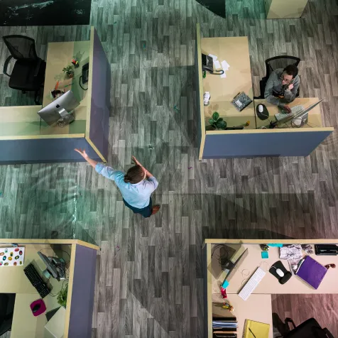 A shot of the set of GLORIA from above, four cubicles sit in a square. There is an individual in the middle of the square gesturing 