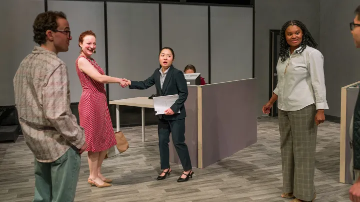 Two people shake hands in the back of the image, while two others look off at the person who has just entered the room